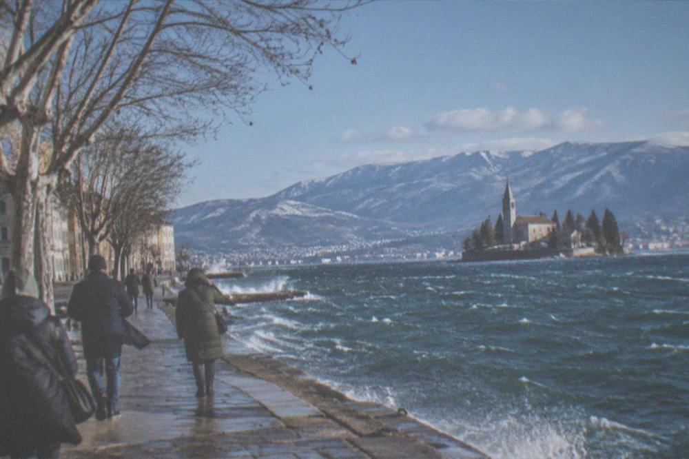 A snowy lakeside town with a church on an island and mountains behind, seen from a viewpoint
