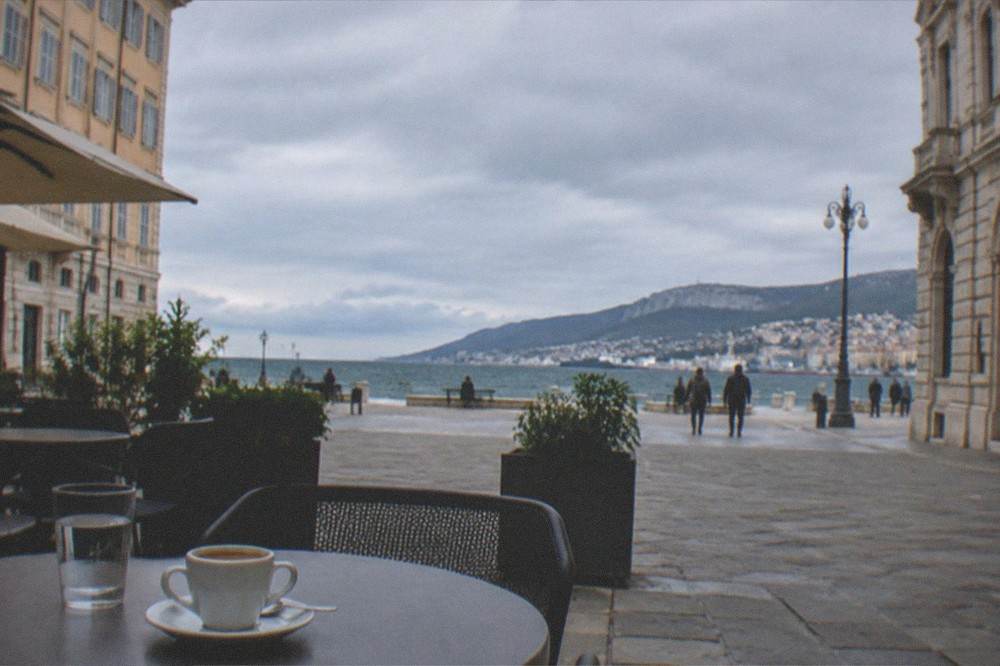 A morning espresso on a cafe terrace with the seafront and distant hills across the gulf in the background