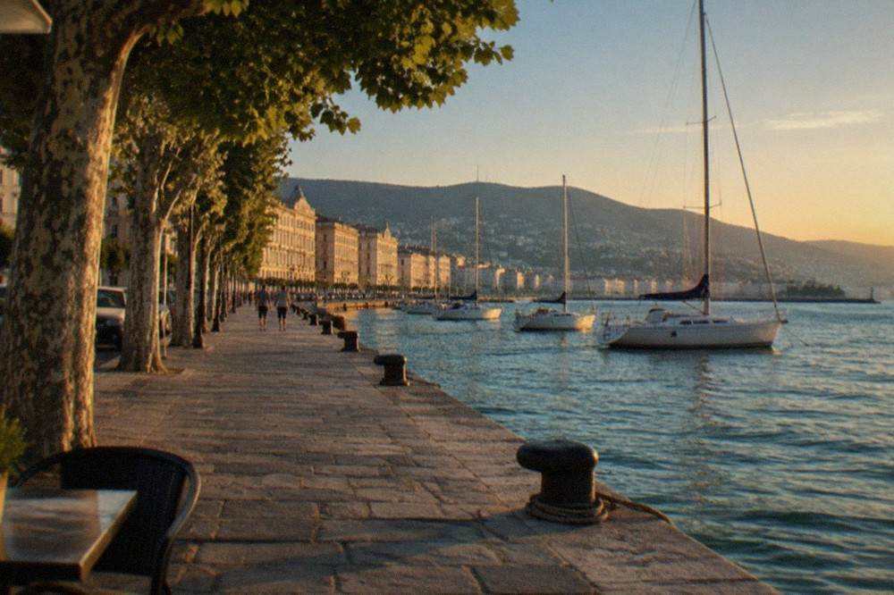 The Rive seafront promenade in Trieste with moored sailing boats and the hills of the Carso in the distance