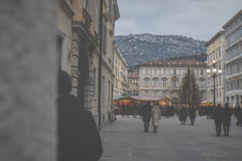 Festive lights strung above an evening market crowd in a European square with a lit tree