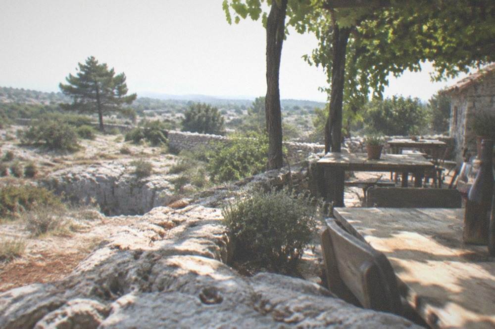 A rustic farmhouse terrace on the Karst plateau with wine bottles and simple wooden tables under vines