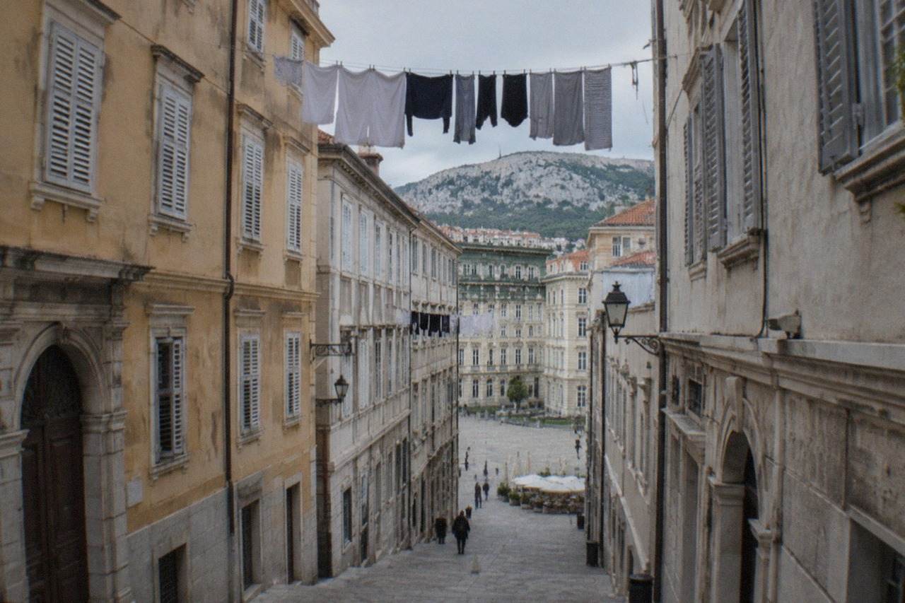 A quiet narrow street in old Trieste with stone buildings and laundry overhead