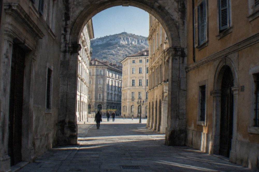 An old stone archway standing between tall houses on a narrow Trieste street