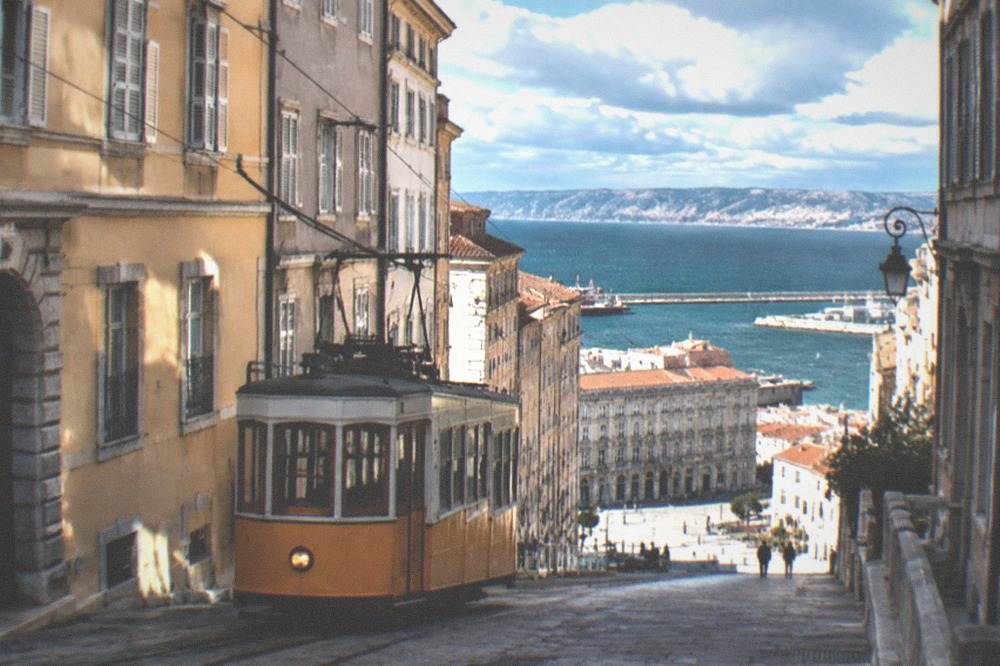 A vintage tram climbing a steep hillside above a coastal city with the sea in the distance