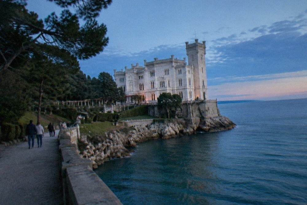 Visitors walking through the free public park of Miramare Castle near Trieste, with the white castle above the sea