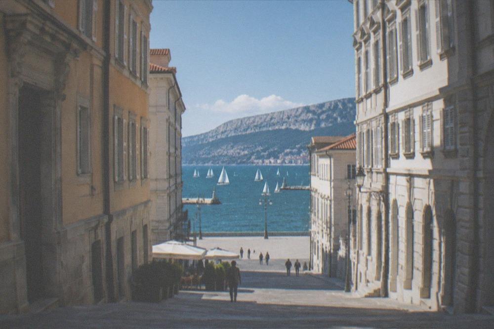 A fleet of white sails spread across the deep green-blue Gulf of Trieste from the seafront