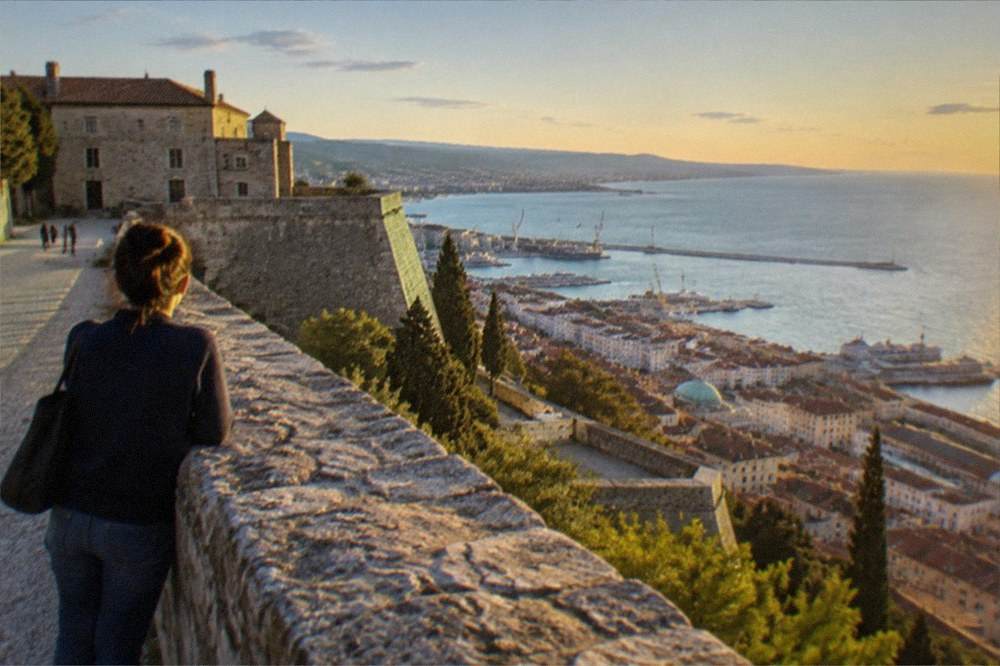 A visitor looking out over the Gulf of Trieste from the walls of Castello di San Giusto at golden hour