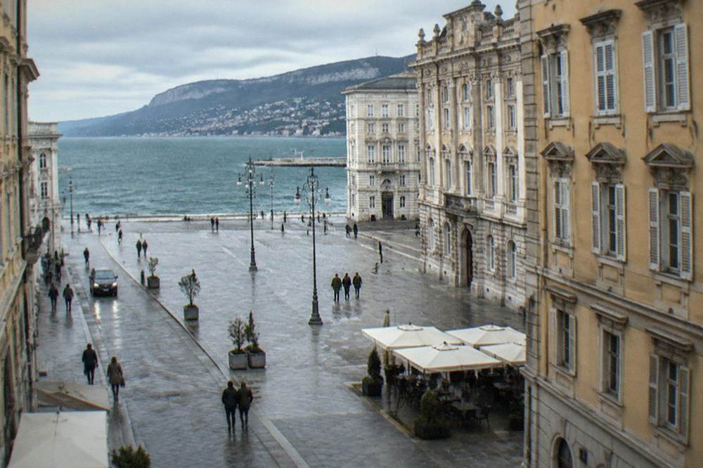 A grand European square with ornate government facades and an open side facing the sea