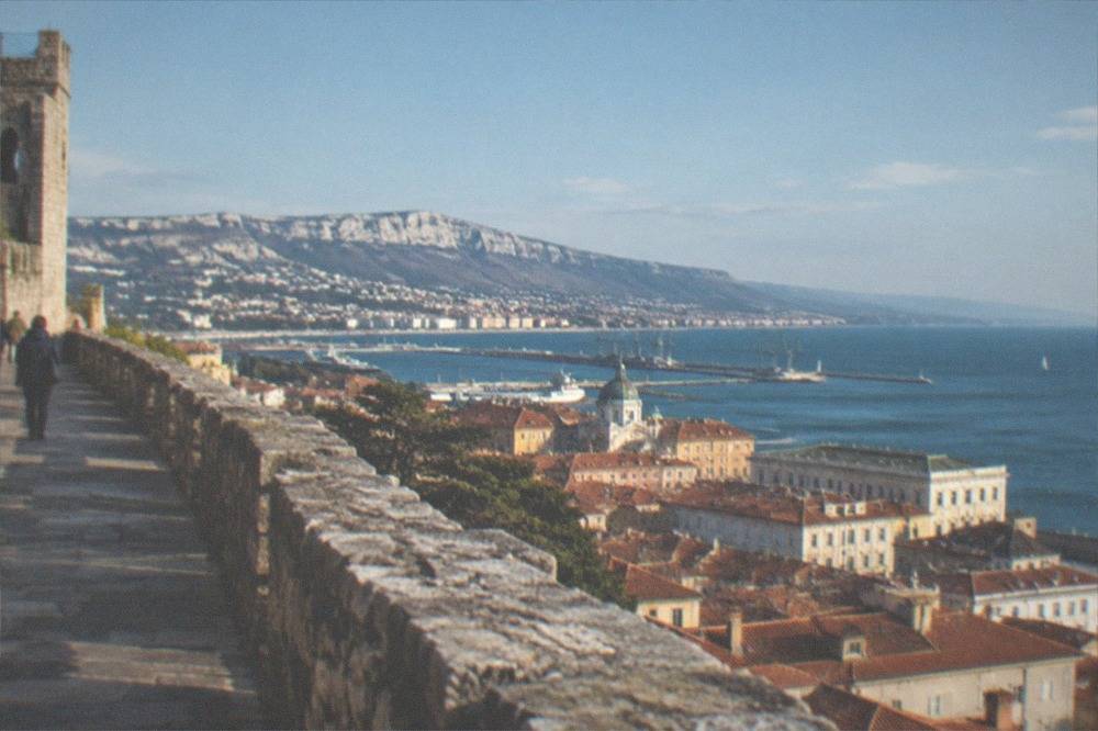 A medieval castle rampart walk overlooking red rooftops and a wide Adriatic gulf