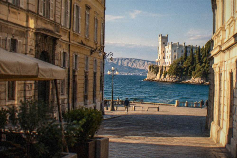 A white seaside castle on a headland above dark blue water with a park of cypress trees
