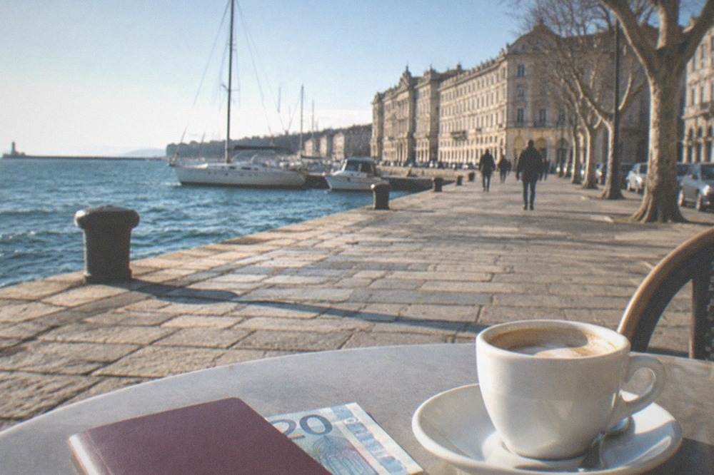A euro banknote and passport resting on a café table beside a cup of coffee