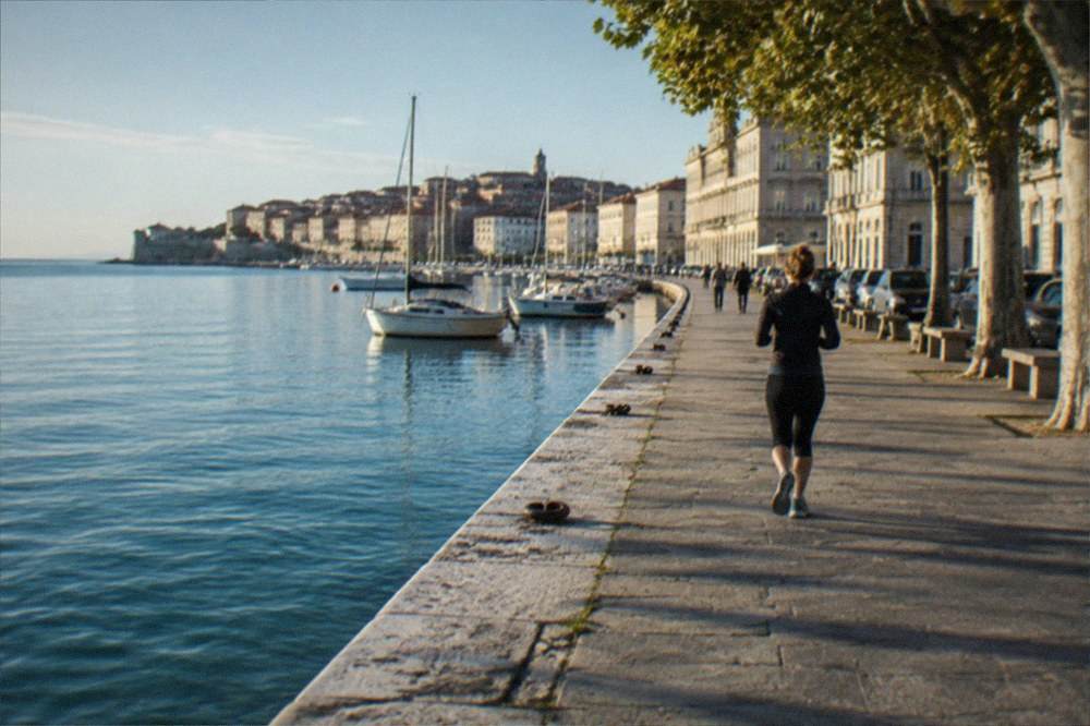 A walled seaside town on a peninsula with terracotta roofs reflected in still evening water