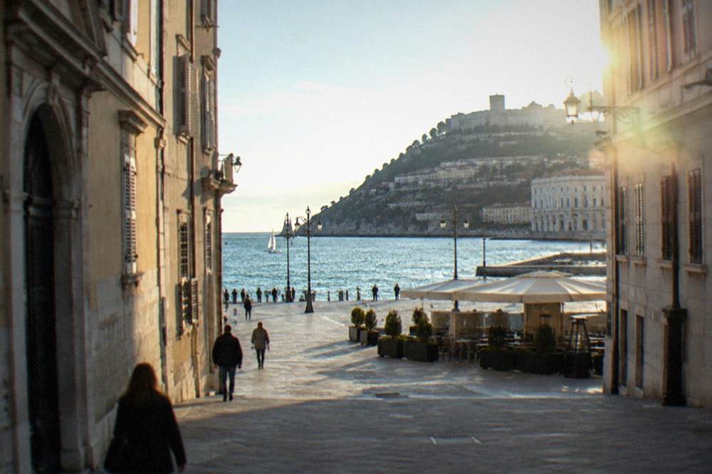 A hilltop castle with defensive walls above the rooftops and the sea beyond
