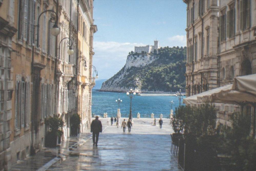 A white clifftop castle above a wooded park and the blue Adriatic