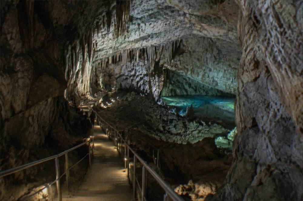 A vast dimly lit cave chamber with a walkway descending into it