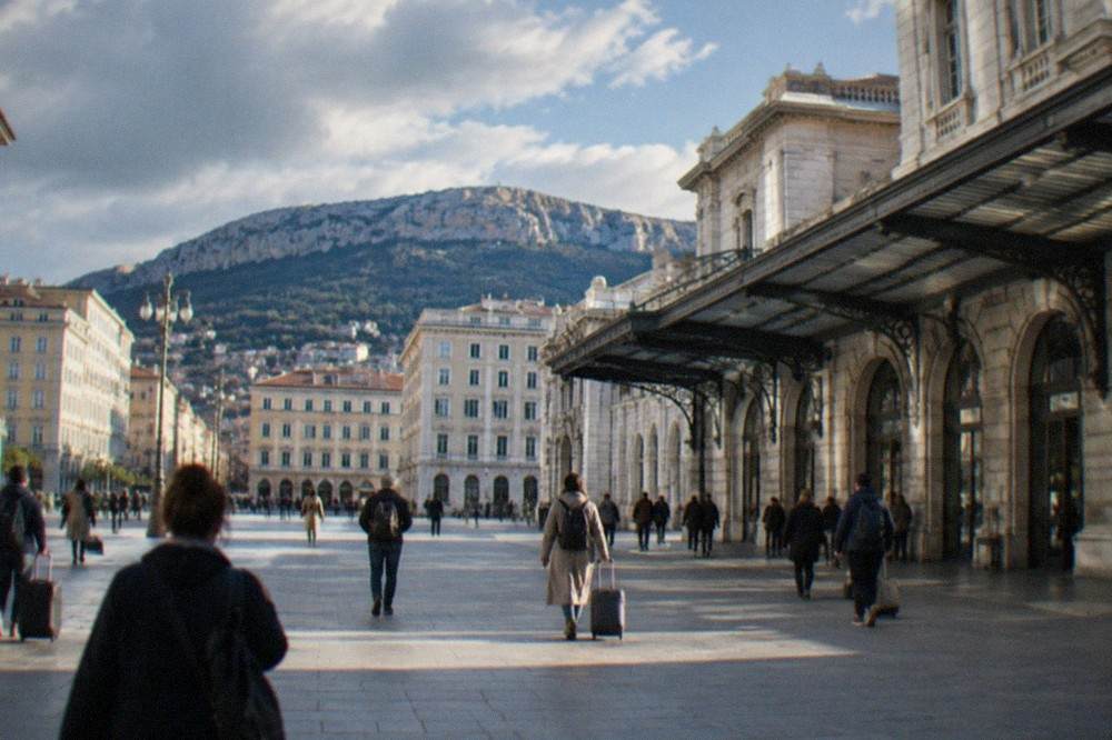 Travellers walking across the open concourse of Trieste Centrale station beneath departure boards
