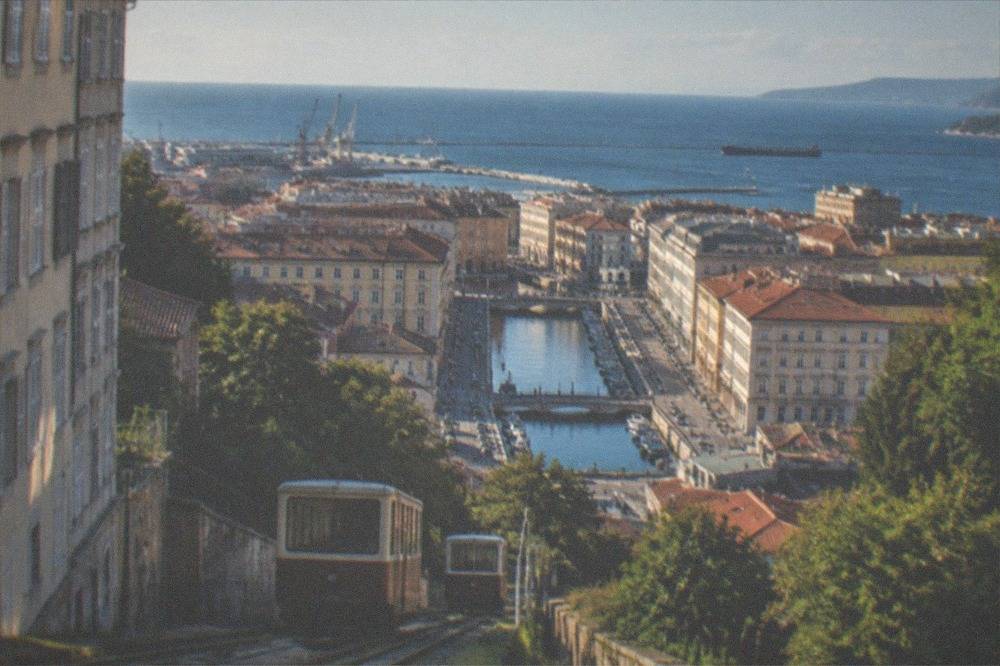 A two-car tram climbing a steep hillside track above a coastal city with a wide sea view
