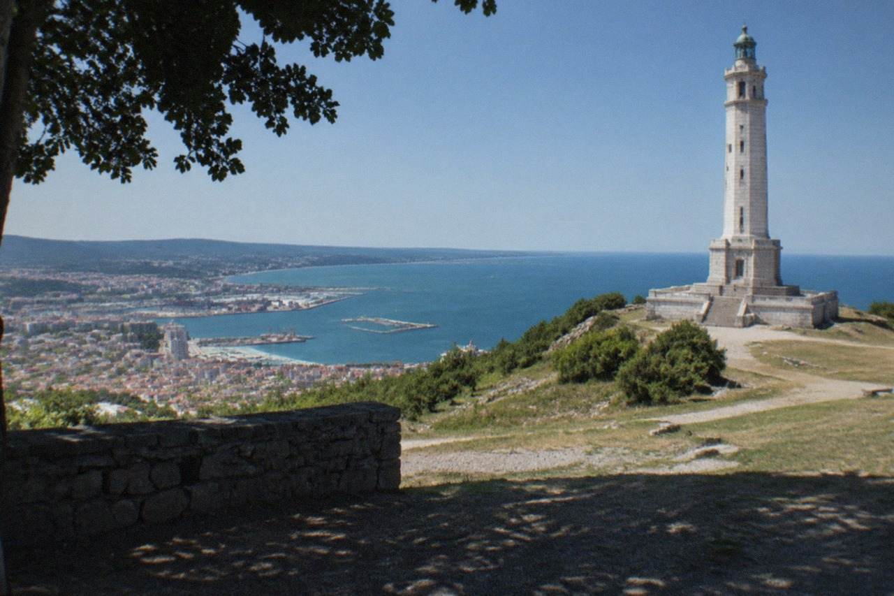 The seafront of Trieste under a clear sky, with the victory lighthouse and the Gulf of Trieste in the distance