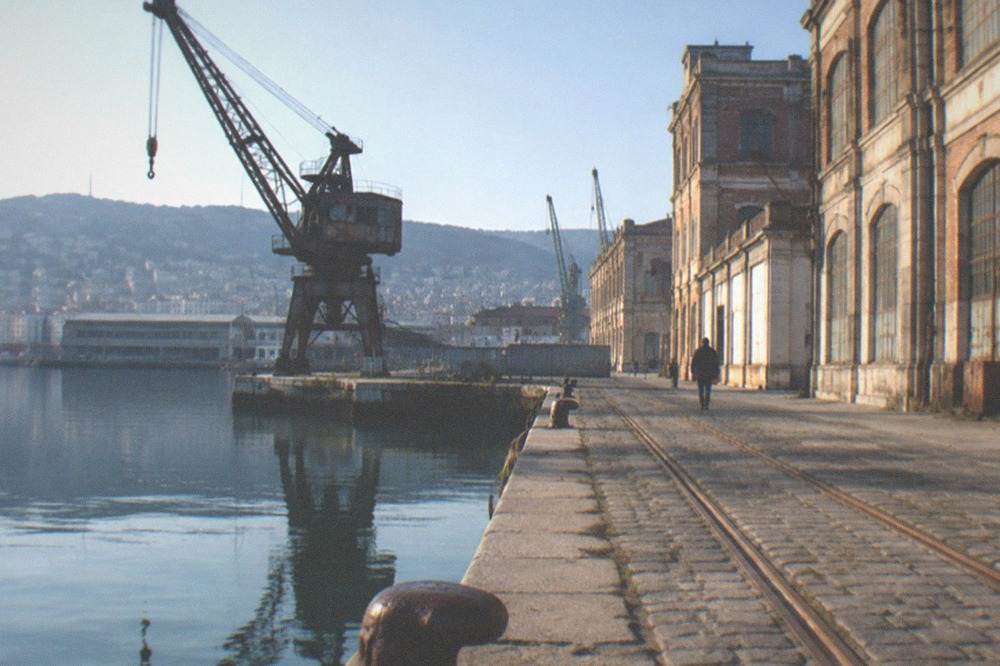 Tall brick and concrete port warehouses with old cranes beside a dock basin in the Old Port of Trieste