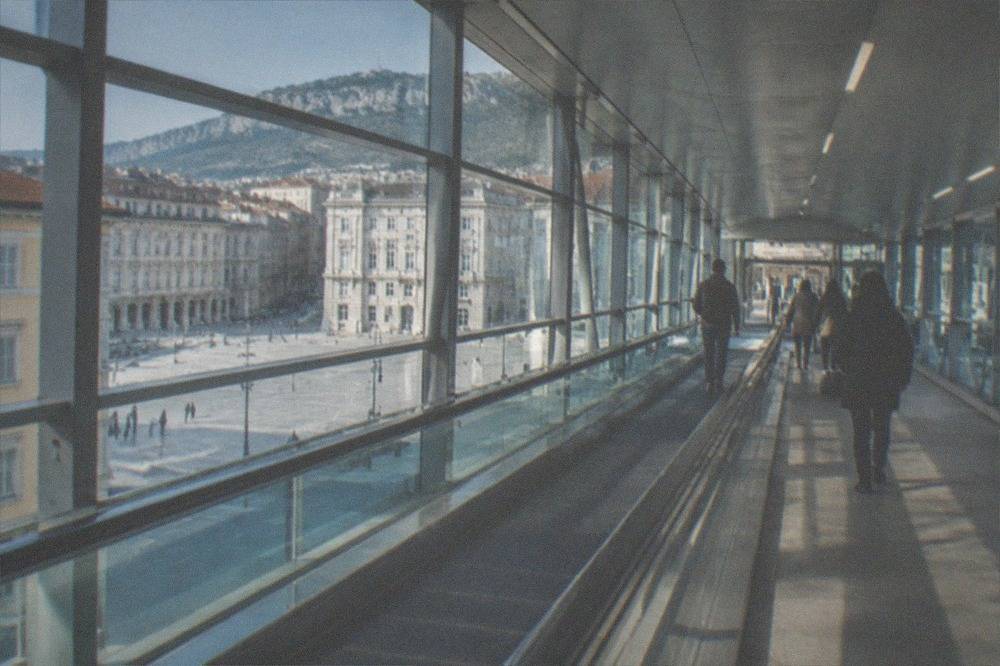 A covered airport walkway with moving walkways connecting a terminal to a railway platform