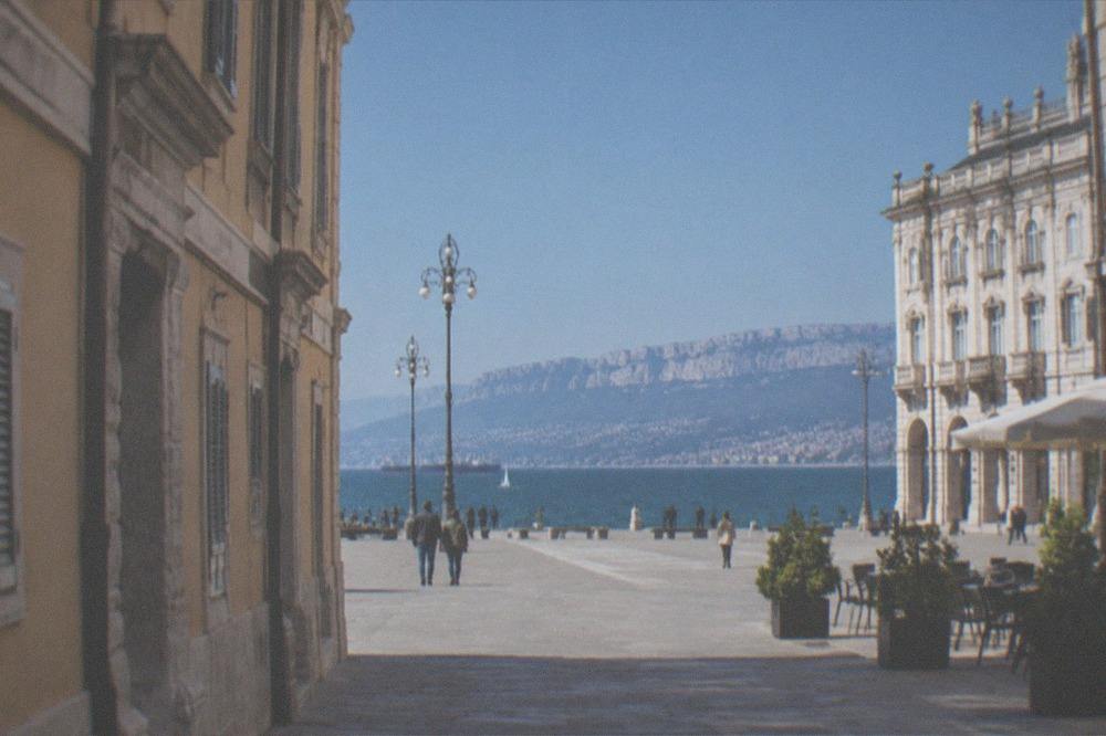 A wide European square facing the sea with ornate facades and open sky above the water
