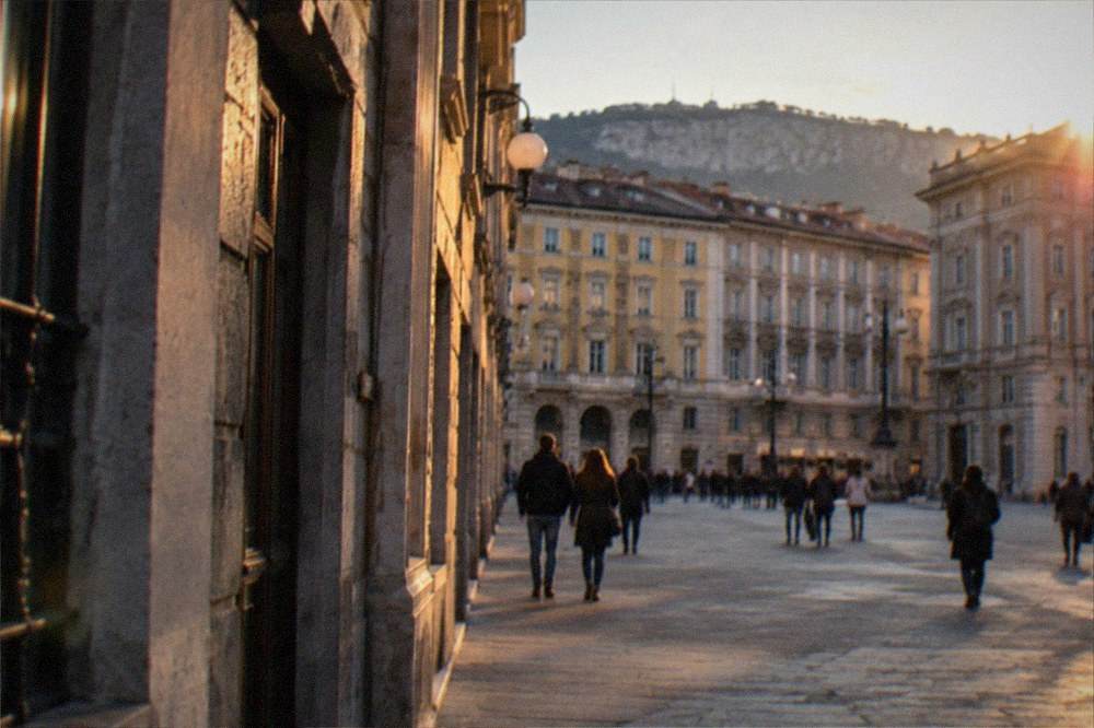 A historic city square at dusk with lit facades and people walking across the paving