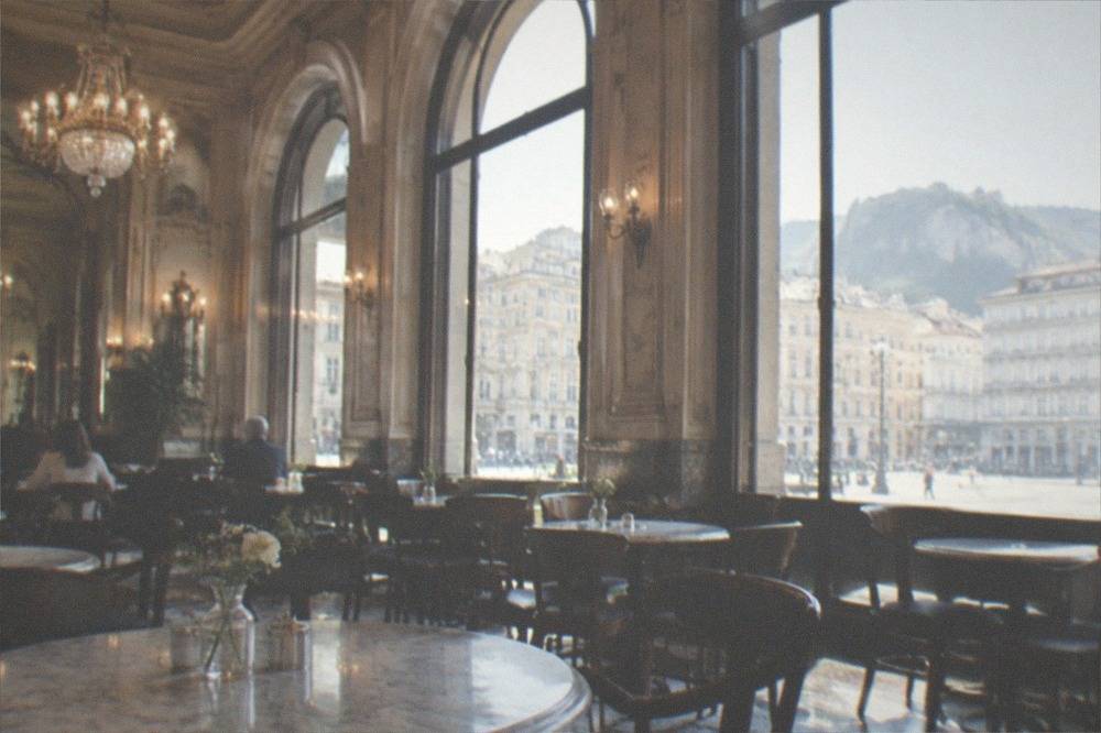 Interior of a grand historic coffee house with marble tables, chandeliers and newspapers on racks
