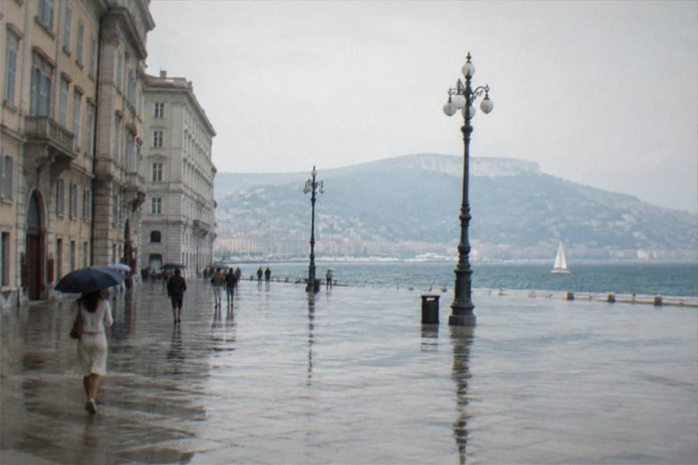 Rain-slicked paving of a large seaside square in Trieste with the sea and hills behind