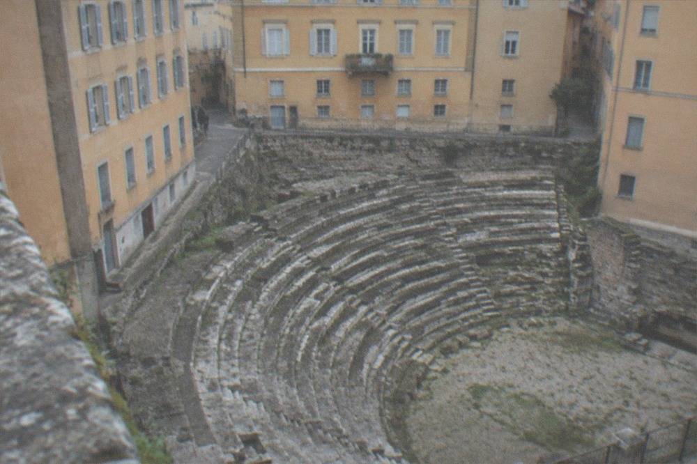 Ancient stone steps of a Roman theatre set between narrow city buildings