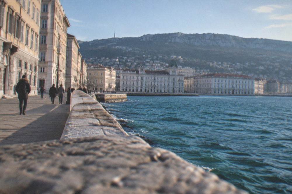A coastal road with a low sea wall and people walking by the water