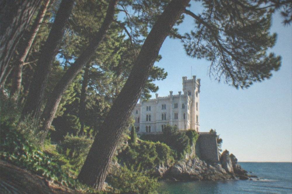The white facade of Miramare Castle above the sea at Grignano, seen through the trees of the castle park