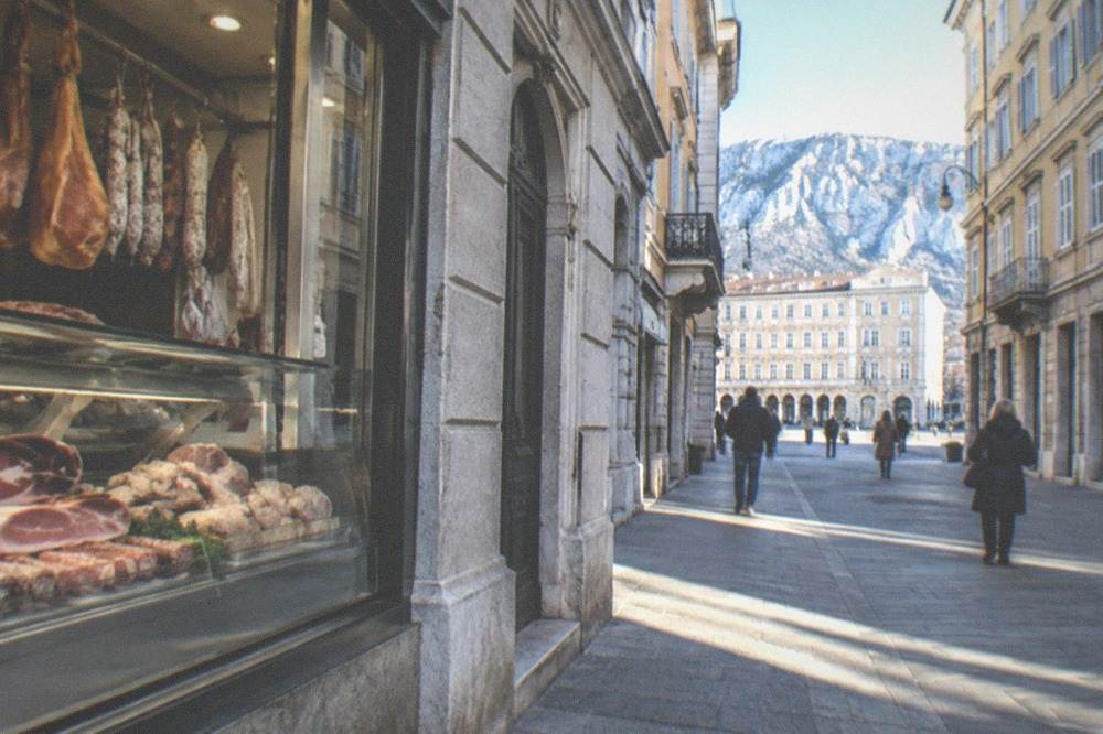 A buffet counter in Trieste with hams, sausages and boiled pork under glass, and a chalkboard menu