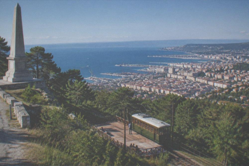 The wooden platform and rail stop of the Opicina tram on a slope above Trieste, with the city and gulf below