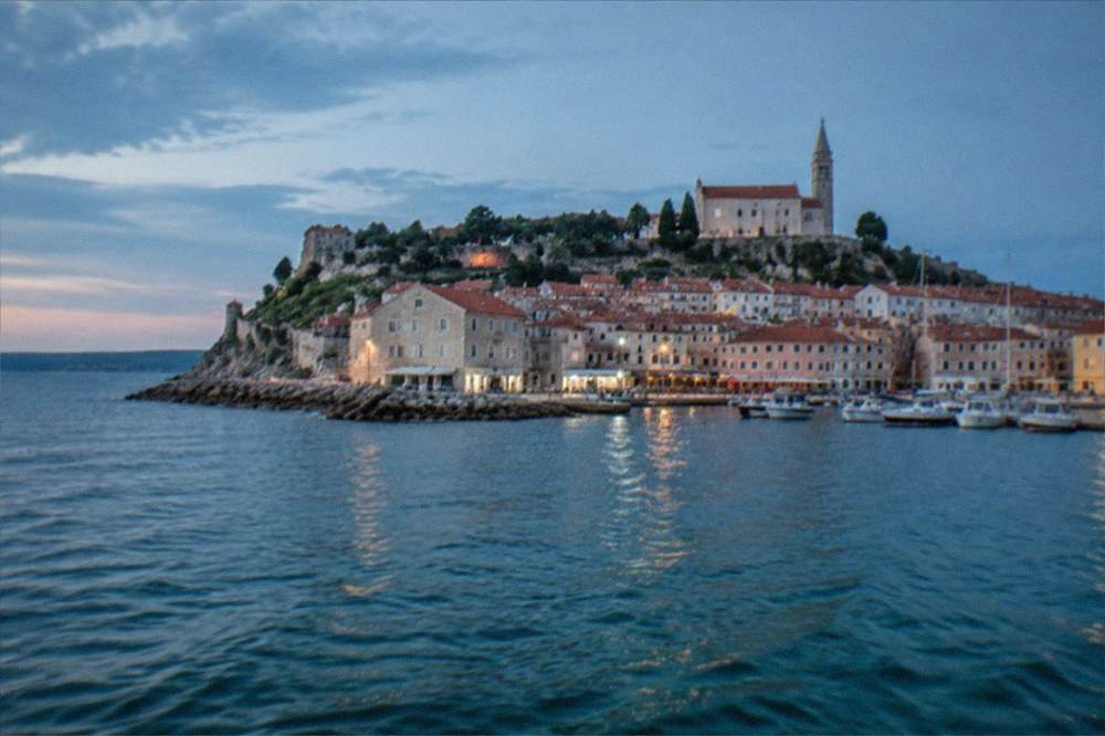 The walled headland of Piran seen from the water, with terracotta roofs above a small Adriatic harbour