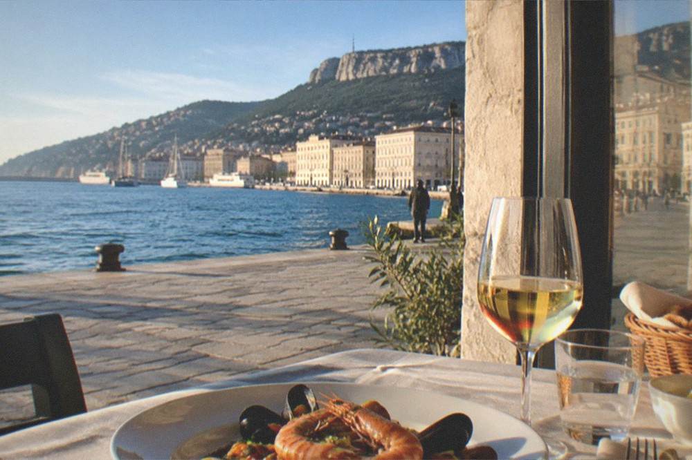 A laid table with seafood and a glass of white wine beside a window overlooking the sea