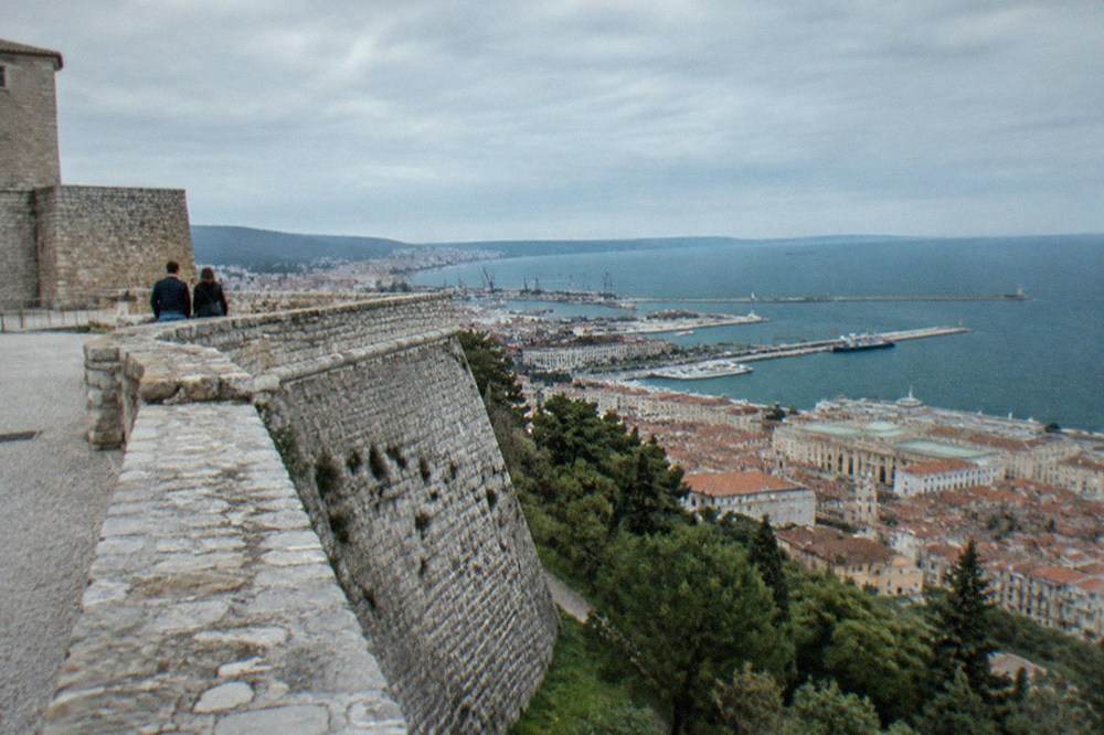 A couple looking out from the castle ramparts on San Giusto hill over the rooftops of Trieste and the Adriatic gulf