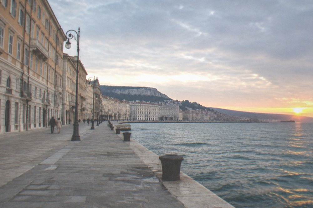 The long stone seafront of Trieste at sunset with the sea on one side and the city facades on the other
