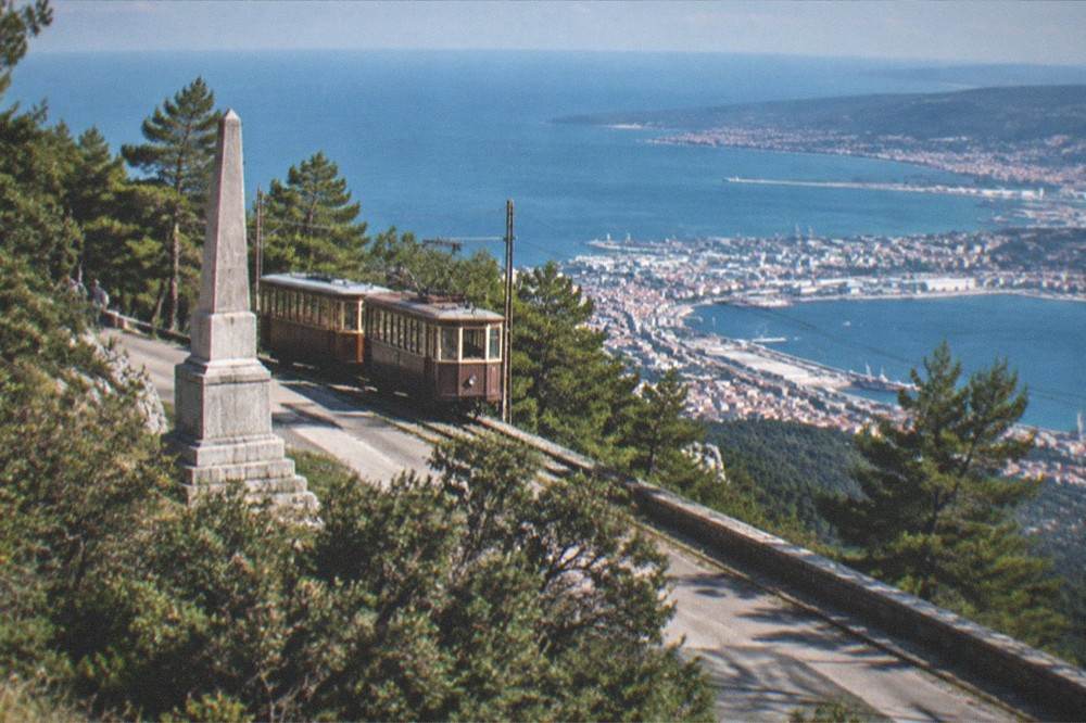 The vintage two-carriage Opicina tram at the upper terminus with the Karst plateau and the gulf behind it