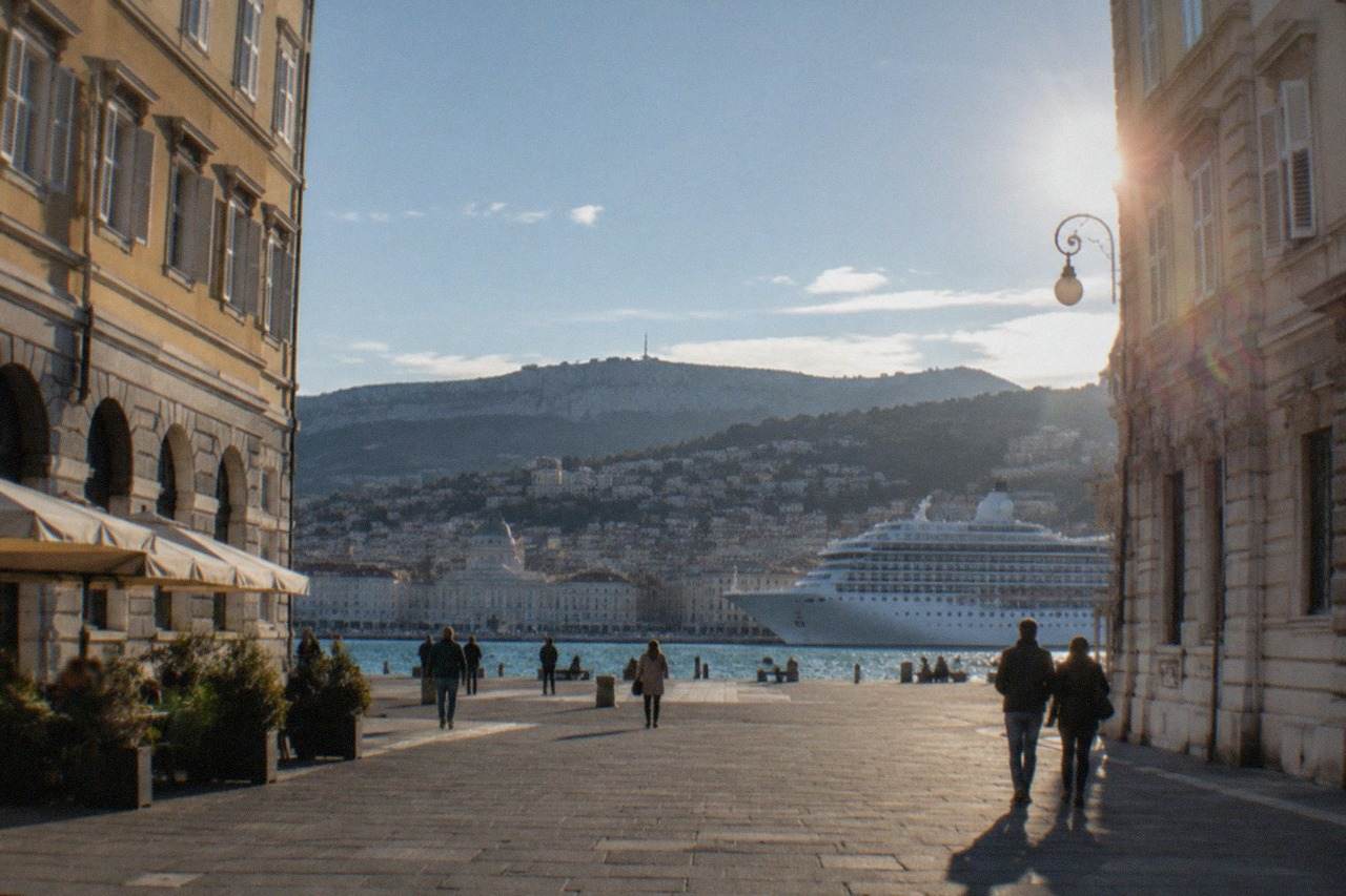 A cruise ship moored at the Trieste waterfront with the seafront and city behind it