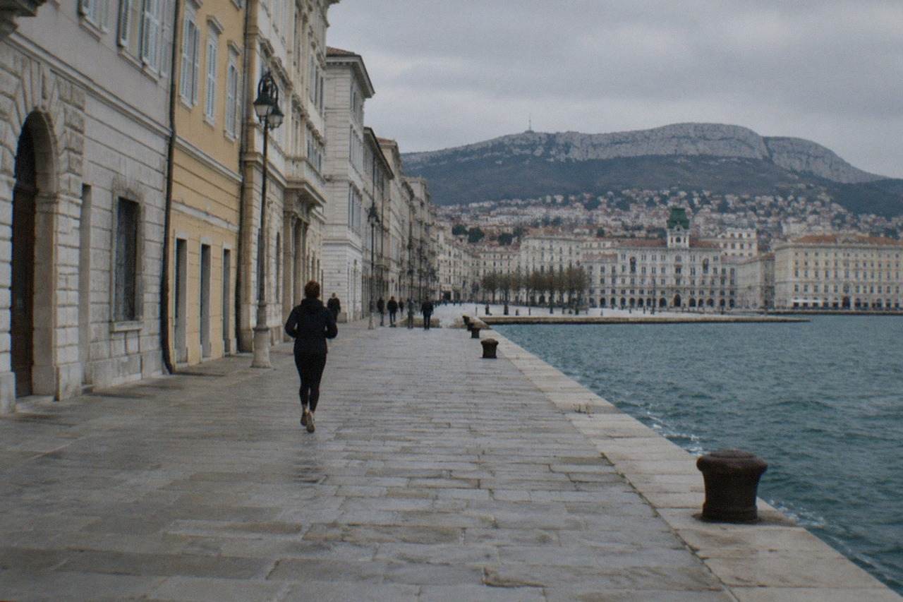 A lone traveller looking out over the sea from the wide stone waterfront of Trieste in Italy