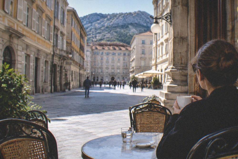 A single visitor with a coffee sitting at a marble table in an ornate historic cafe in Trieste